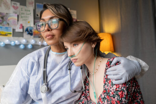 Young nurse in protective wear embracing the sad sick girl, she supporting her during disease at hospital ward
